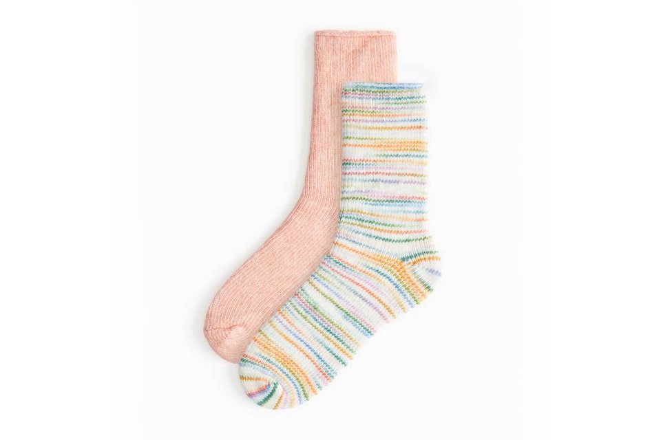 Pair of cosy winter socks, one in solid pink and the other in white with colorful stripes.