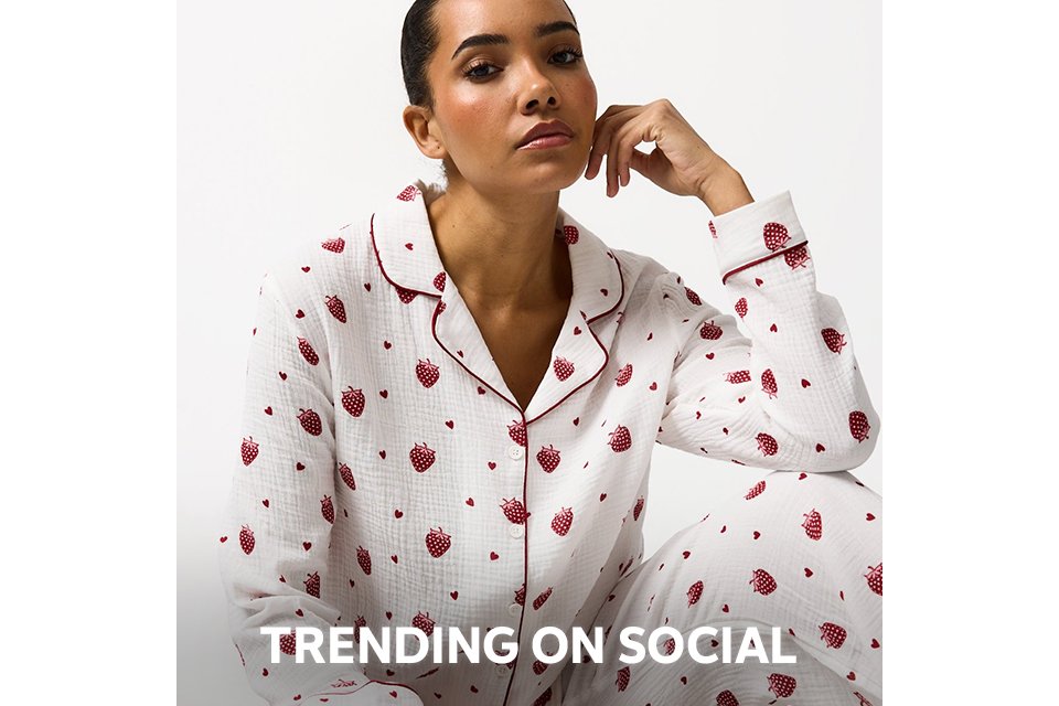 Person wearing a pink and red satin pajama set with a diamond pattern and decorative motifs, paired with beige slippers, standing against a plain white background.