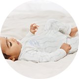 Baby lying down in a white sleepsuit.