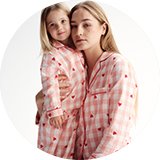 Two people wearing matching pink check pyjamas with red hearts.