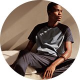 Person sitting in grey top and dark pyjama bottoms.