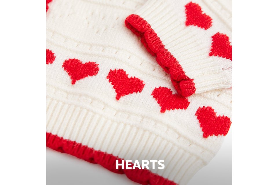 Close-up of cream knitwear featuring red embroidered heart patterns and red trim.