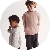 Two children wearing cosy jumpers in neutral tones, standing side by side. 