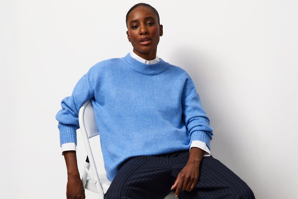 Person wearing a bright yellow long-sleeve crew-neck sweater paired with dark grey jeans, seated on a light-colored surface.