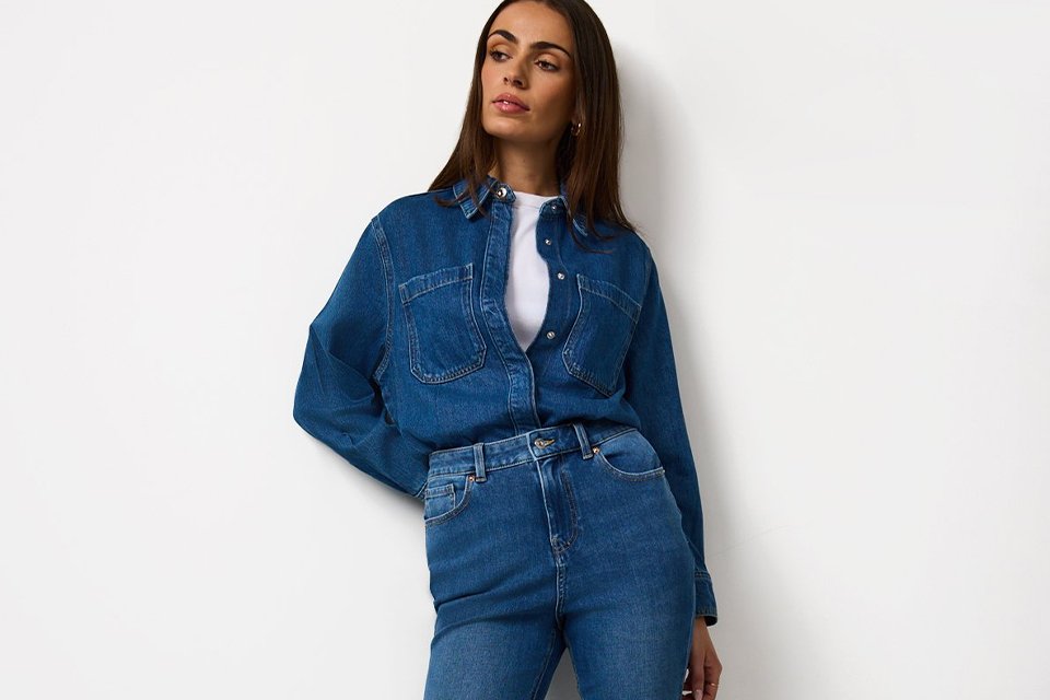 Person wearing a dark denim jacket and matching mini skirt, styled with a white top, blue patterned neck scarf, brown socks, and black loafers.