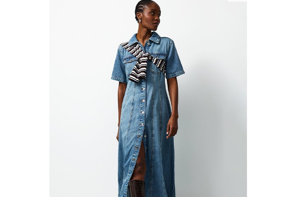 Person wearing a black long-sleeve ribbed top paired with a high-waisted black denim midi skirt featuring a front slit, styled with white sneakers. 