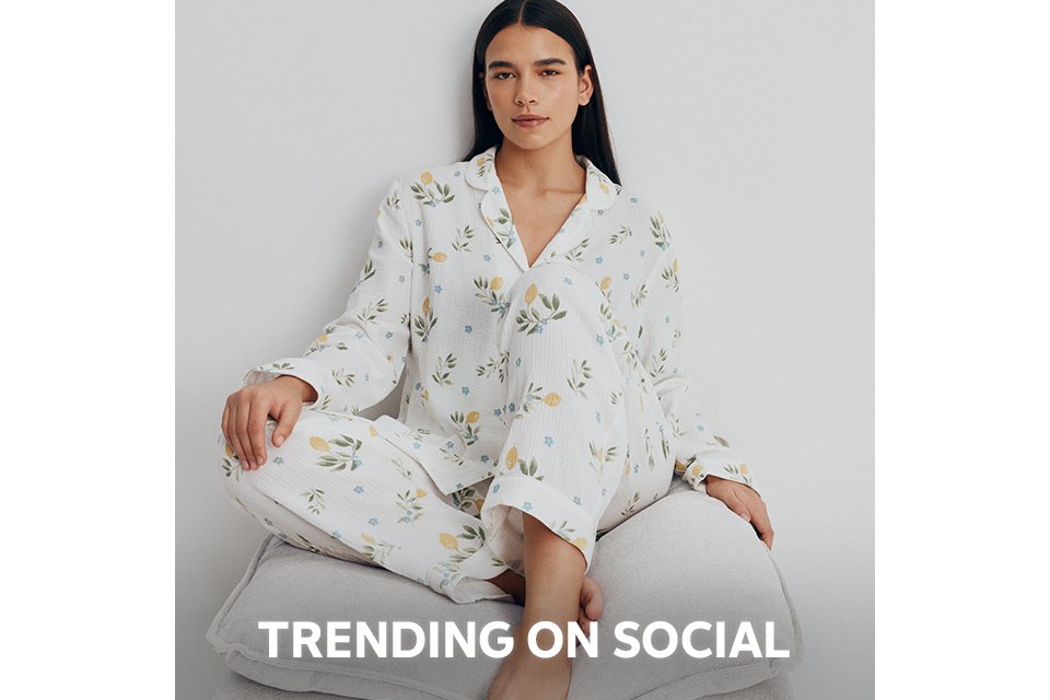 Person wearing a pink and red satin pajama set with a diamond pattern and decorative motifs, paired with beige slippers, standing against a plain white background.