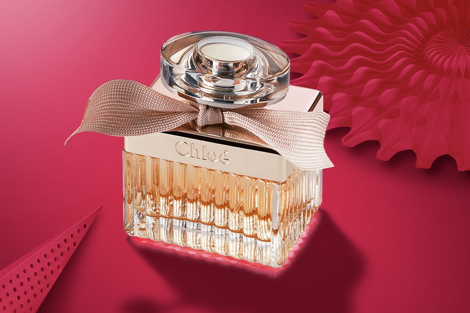 Chloé Eau de Parfum bottle with signature ribbon, styled on a pink background for luxury fragrance gifting.